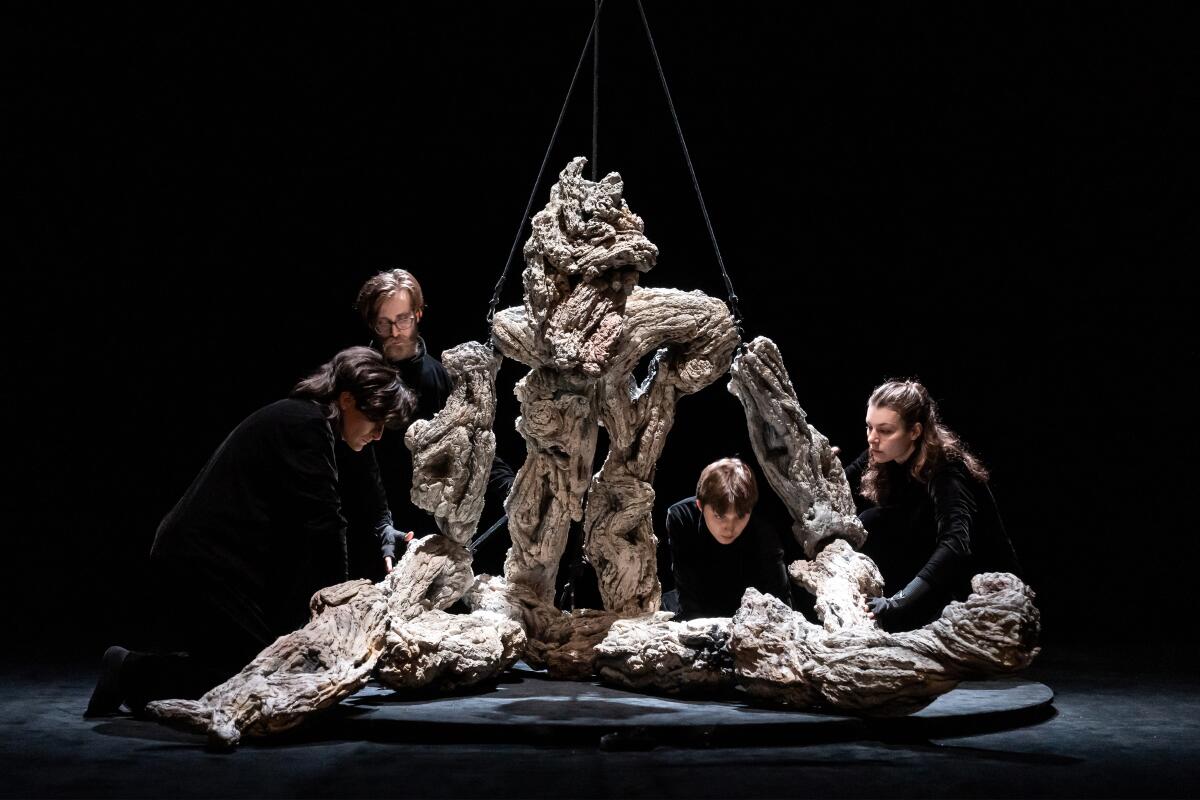 Four puppeteers crouch around a monster-like figure during a scene from "Book of Mountains and Seas."