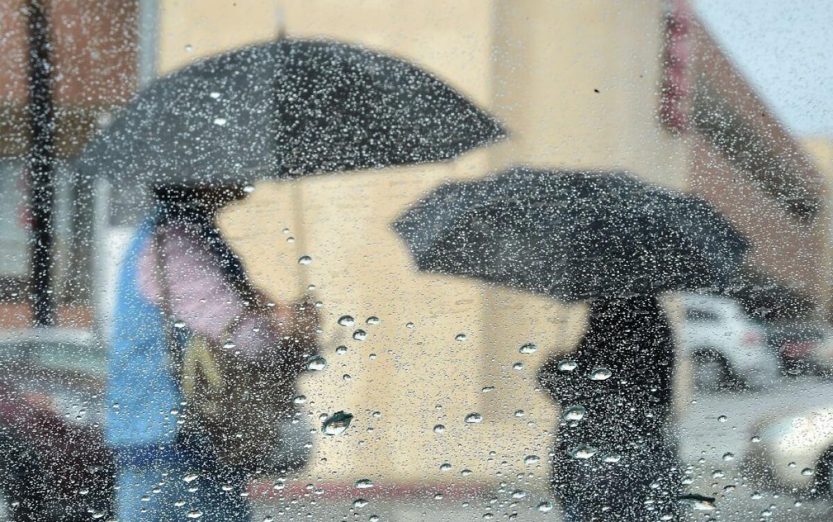 Two women trudge through the morning rain under umbrellas as a storm drenches Southern California.