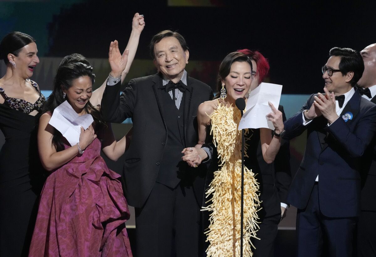 People celebrate on a stage as a woman in a gold and black gown reads a speech.
