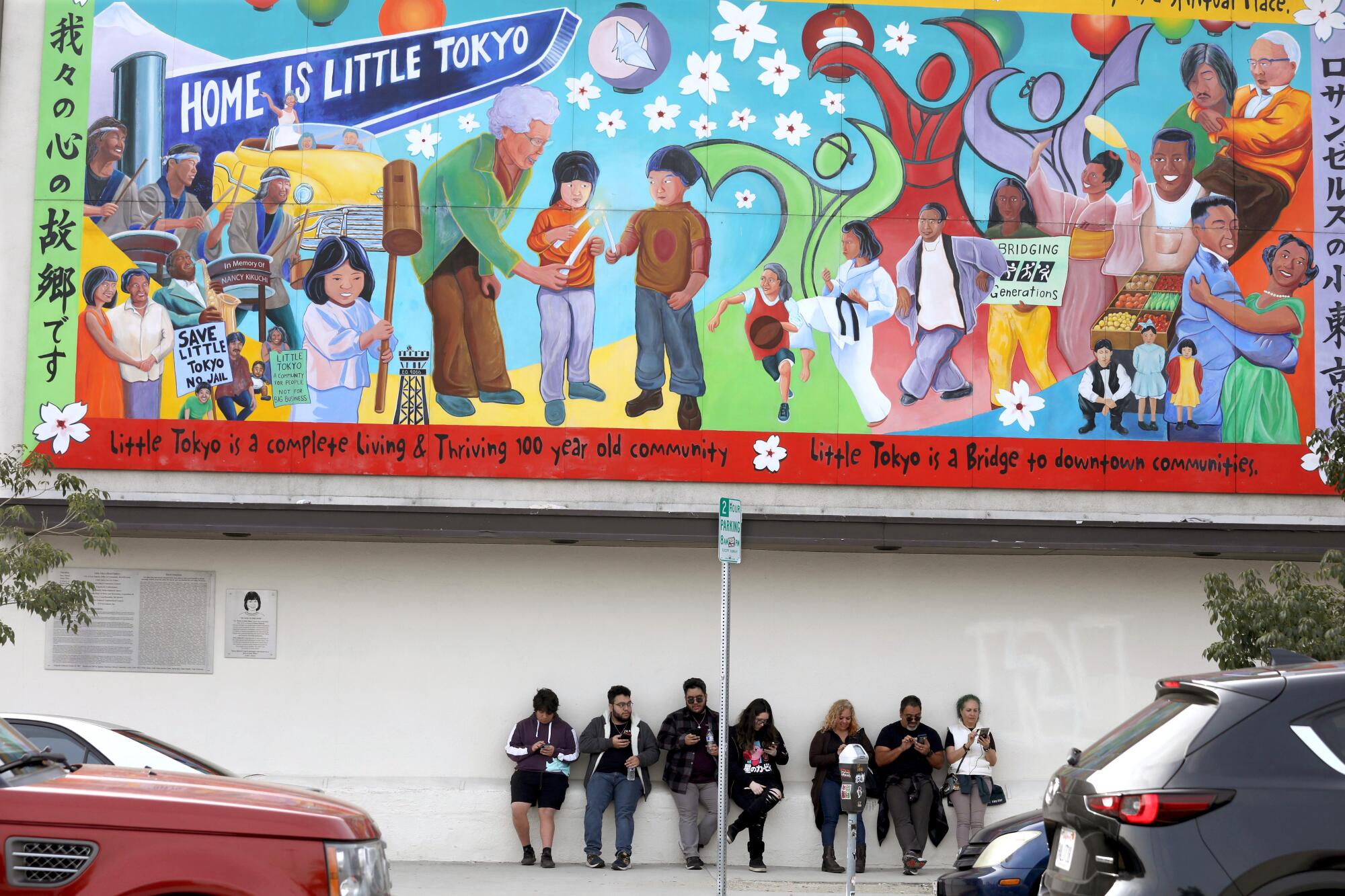 Visitors spend an idle moment together in Little Tokyo under a colorful mural of people.