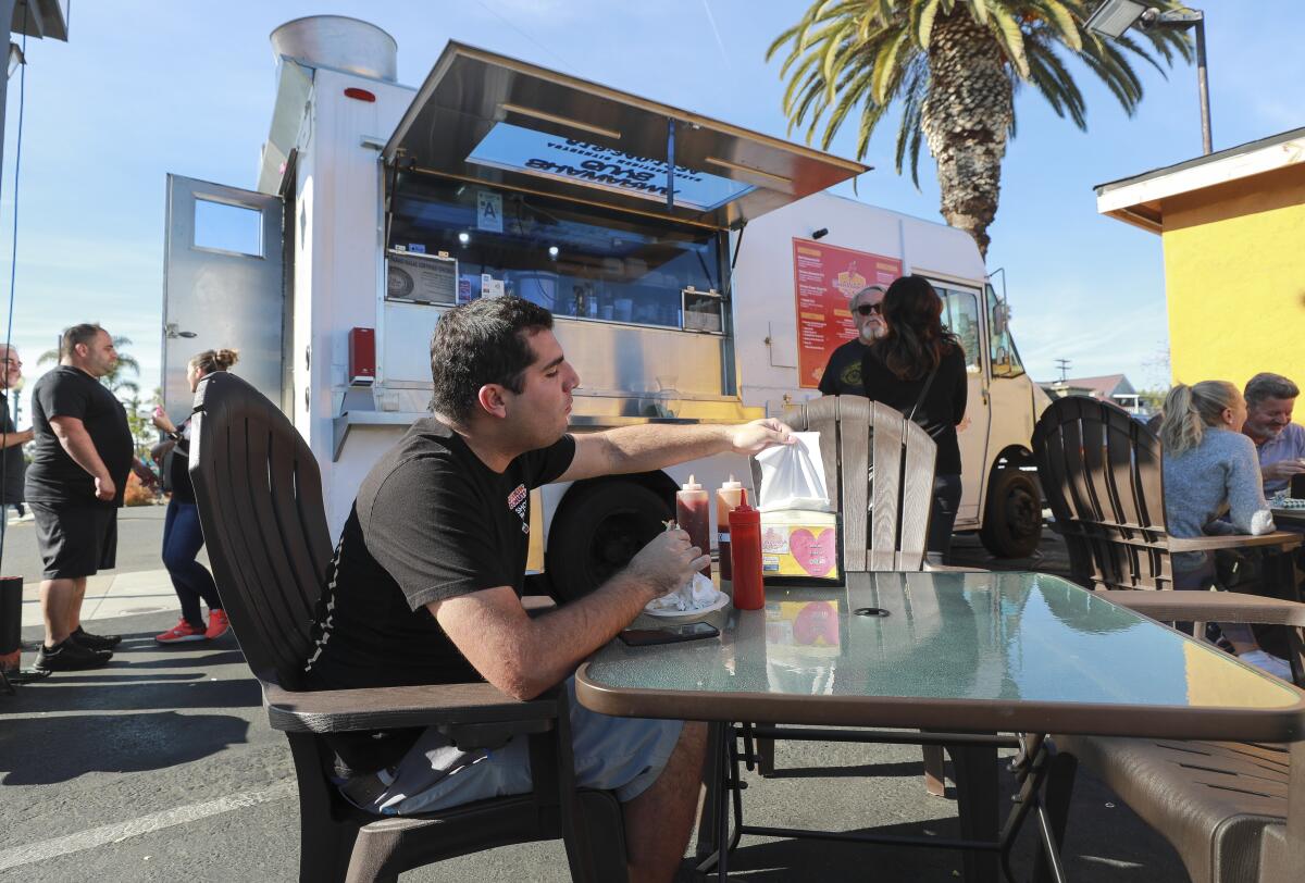 Alex Gómez agarra una servilleta mientras come un pollo shawarma en el camión de comida Shawarma Guys mientras el dueño y chef Bryan Zeto, a la izquierda, está parado afuera de su camión de comida en South Park el sábado 4 de enero, San Diego.