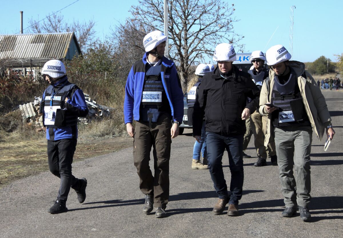 Deputy Head of the OSCE Special Monitoring Mission, Mark Etherington, second right, and other members of OSCE walk through a street near a frontline in Petrovske, Ukraine, Wednesday, Oct. 9, 2019. At least one Ukrainian police officer has been injured in scuffles between police and activists who have arrived to the frontline in eastern Ukraine to derail the pullback of government forces. (AP Photo/Alexei Alexandrov)
