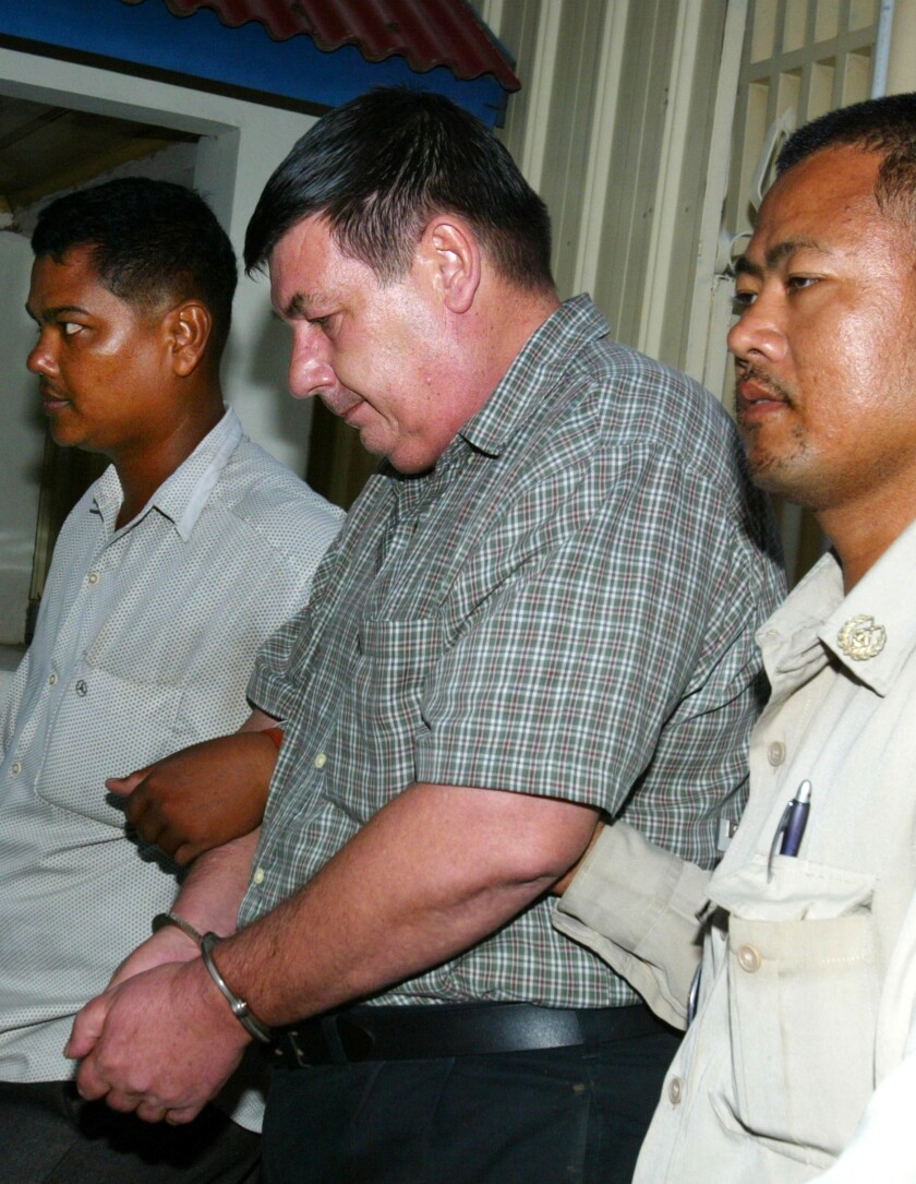 Police walk on either side of a handcuffed man, holding his arms