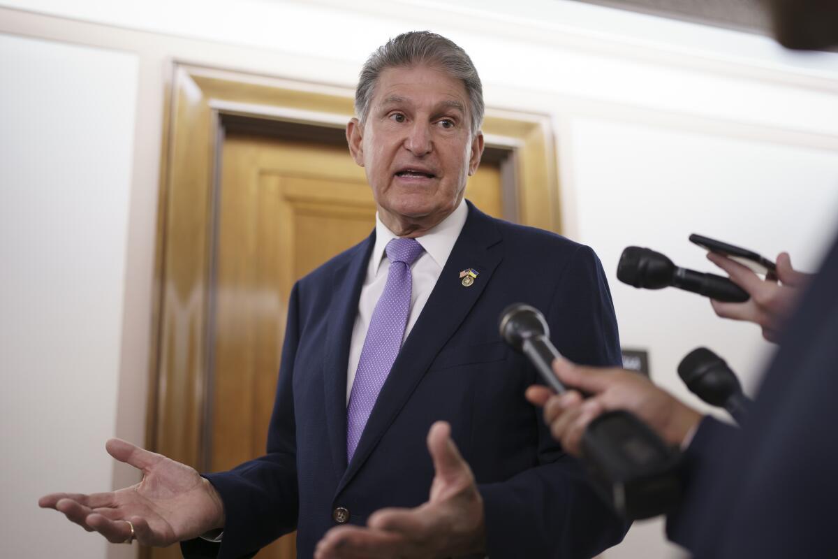 A man in a dark suit gesturing while speaking into several microphones held by off-camera reporters