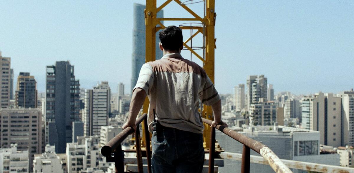 The back of a man on a construction crane in front of a cityscape. 
