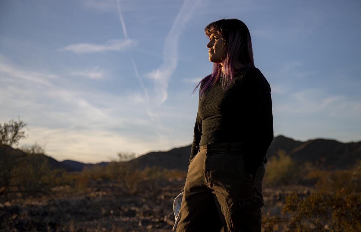 Gina Chavez stands for a portrait, looking into the distance in a desert landscape