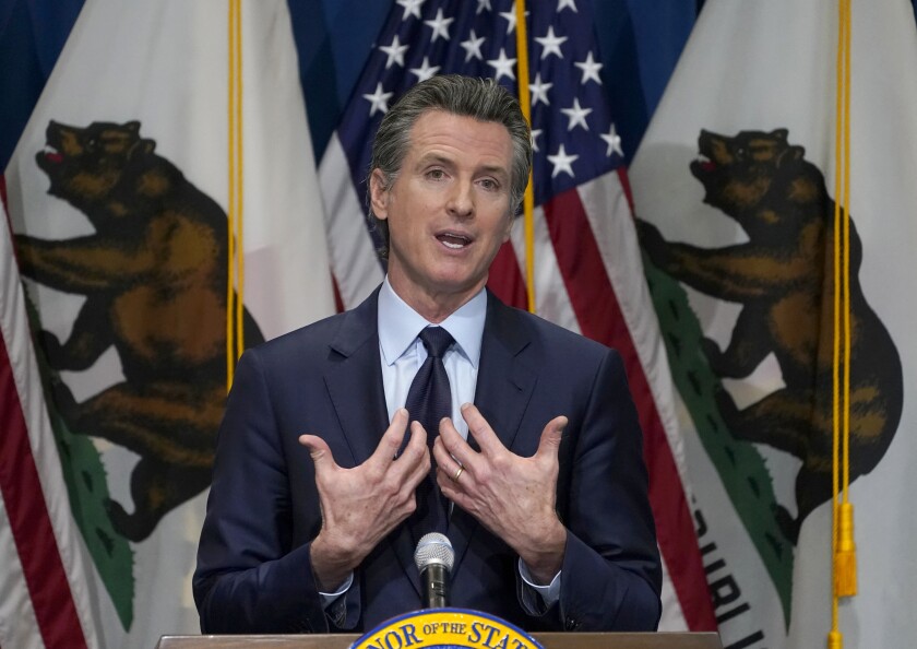 Gov. Gavin Newsom, backed by California Bear Flags, speaks at a podium.