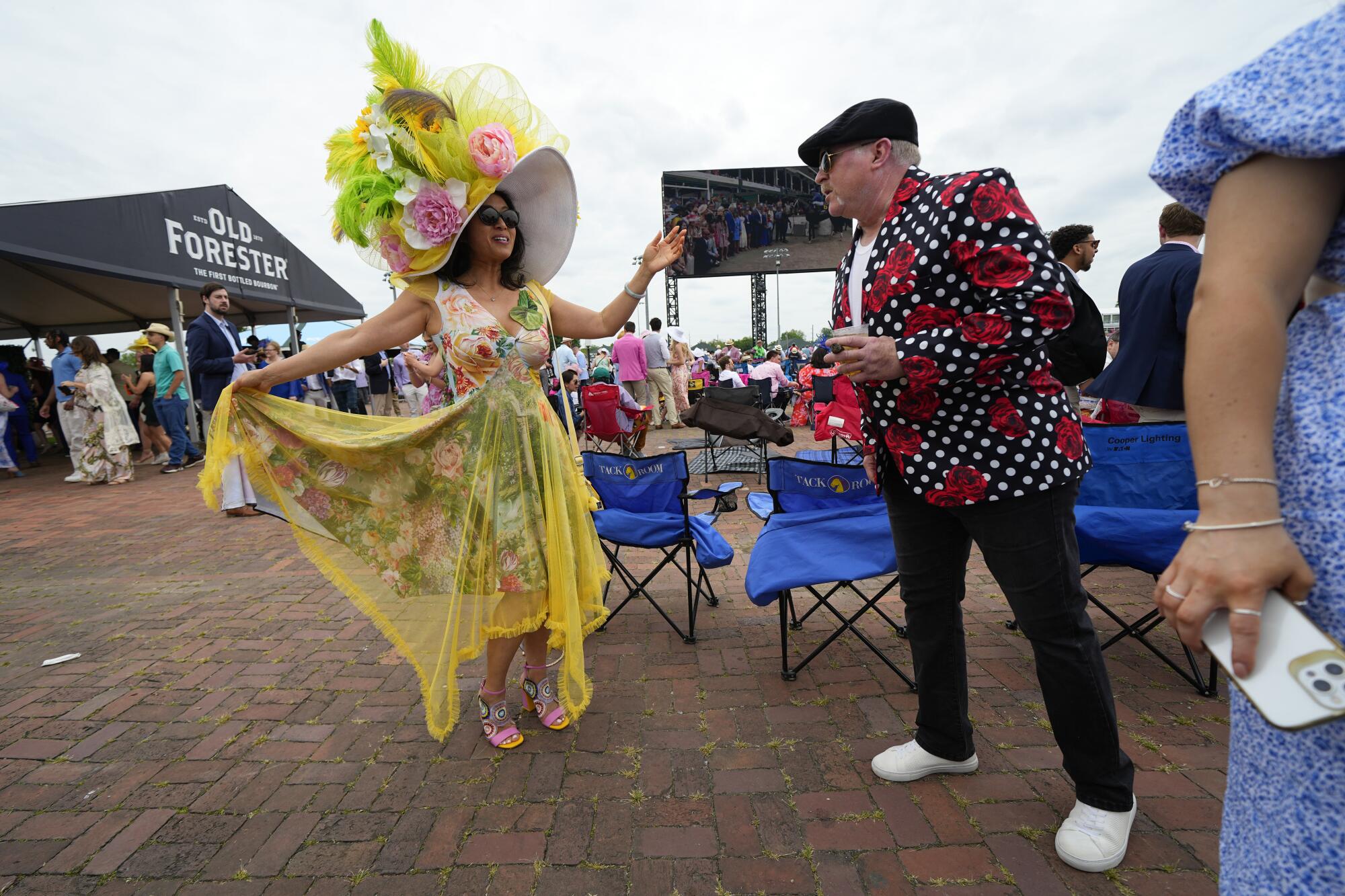 A woman dressed in a tall yellow, green and pink hat stands next to a man at Churchill Downs 