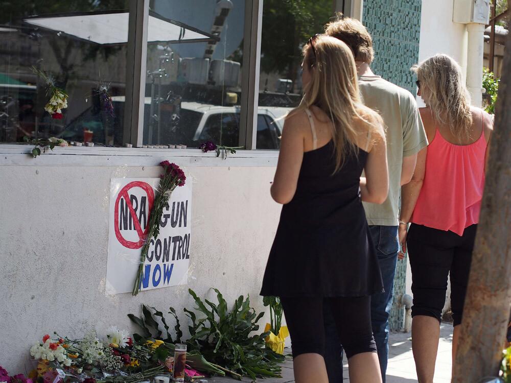 People pause to look at flowers and an anti-gun sign May 25 in front of the IV Deli Mart, in Isla Vista, Calif.