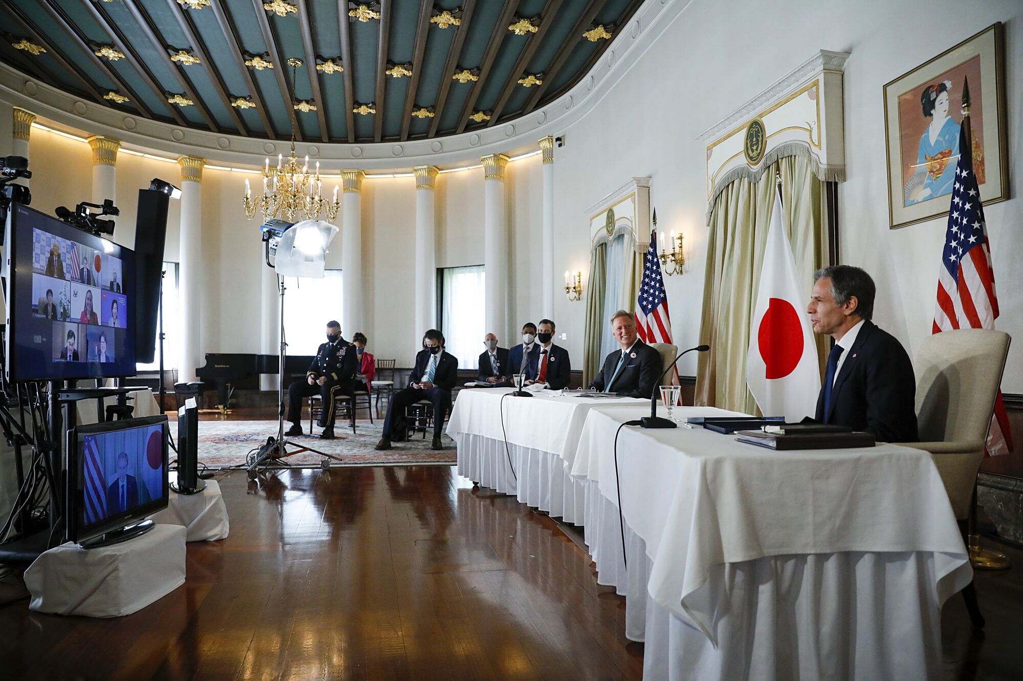 Secretary of State Antony J. Blinken, right, and other officials are seated apart, with U.S. and Japanese flags behind them