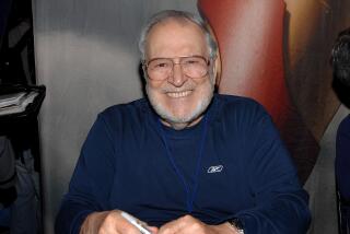 John Romita sits at a table smiling with a pen in his hand