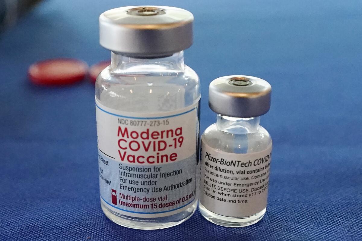 The COVID-19 vaccines made by Pfizer-BioNTech and Moderna sit side by side on a table.