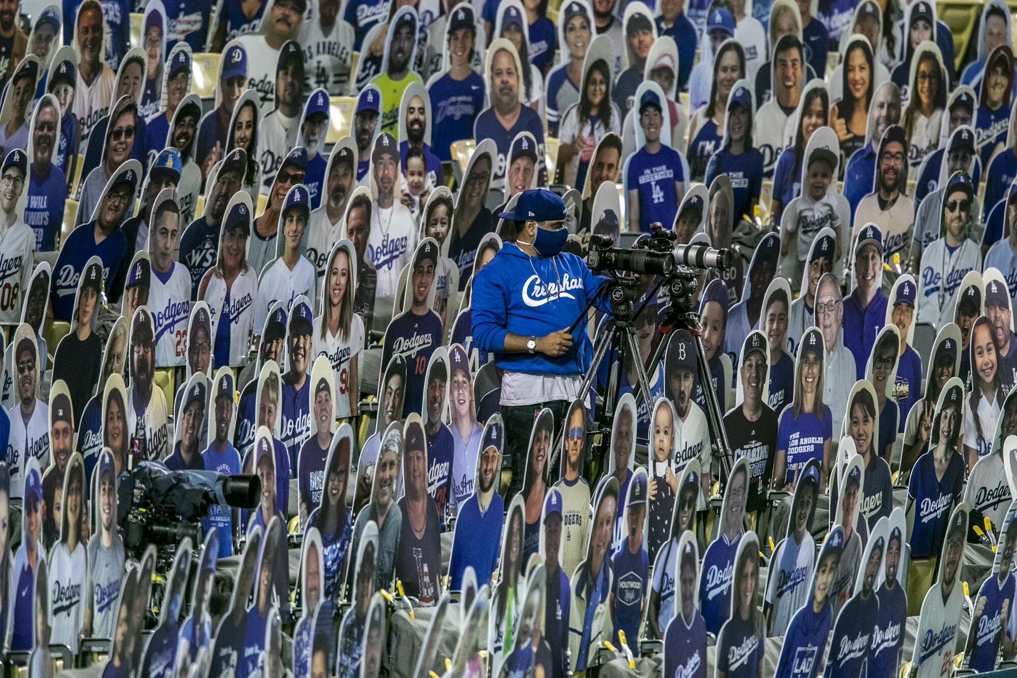 A man and his camera are perched in stadium seating amid numerous cardboard likenesses of fans. 