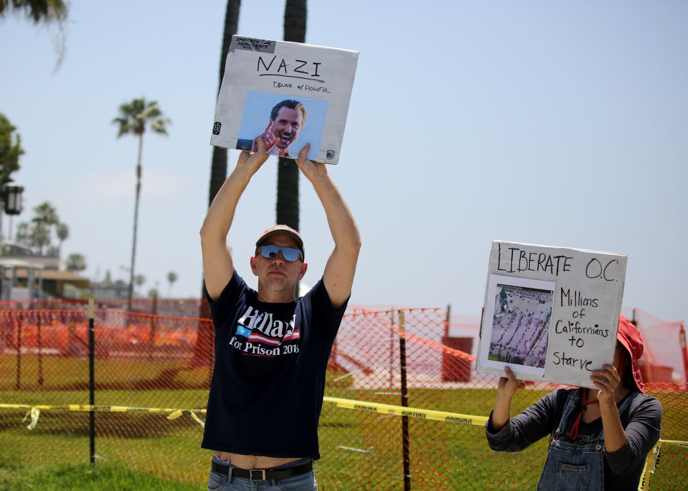 A handful of protesters hold up signs next to rthe fenced-off Main Beach Park in Laguna Beach on Saturday.