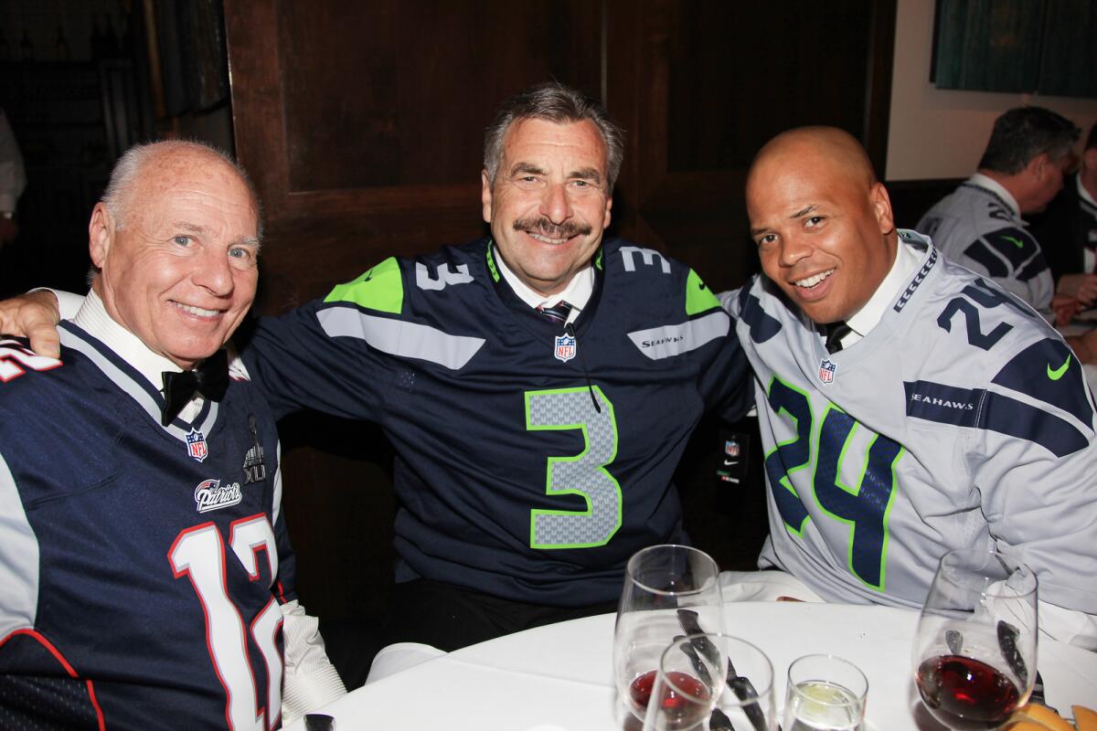 Three men sit at a banquet table wearing football jerseys over their formal attire