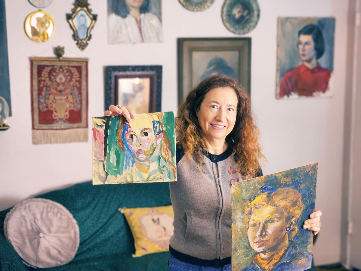 With a portrait in one hand and older art in the other, Sheree Perelman in front of a gallery wall of vintage portraits.
