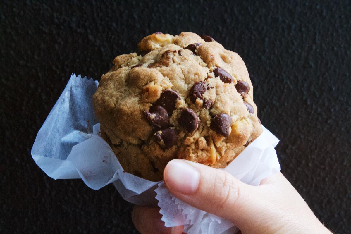 A hand holds a chocolate chip walnut cookie from Levain Bakery Los Angeles against a black wall.