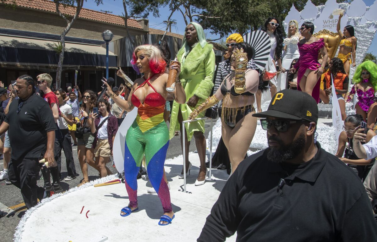 Singer Cardi B stands in a rainbow-colored outfit on a float with other people in bright outfits