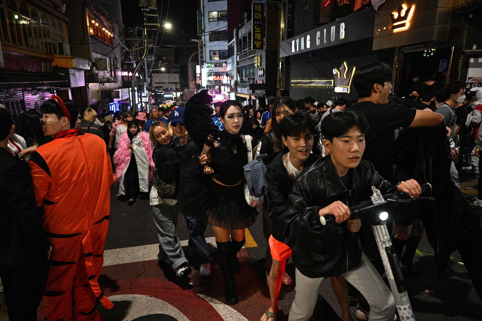Revelers, some in costume, on a crowded street at night 