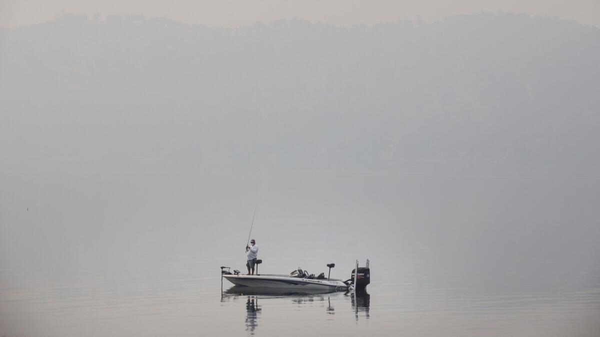 Wearing a protective mask because of poor air quality, a man fishes in Clear Lake as the smoky haze shrouds visibility.