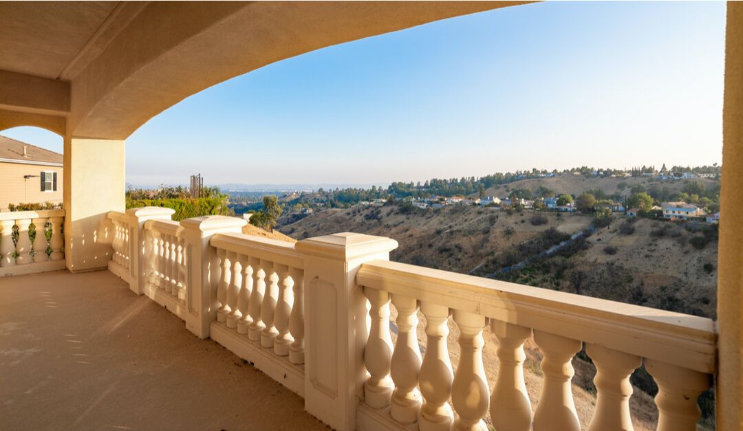 A balcony with elaborate concrete banister has views of the Valley hills.