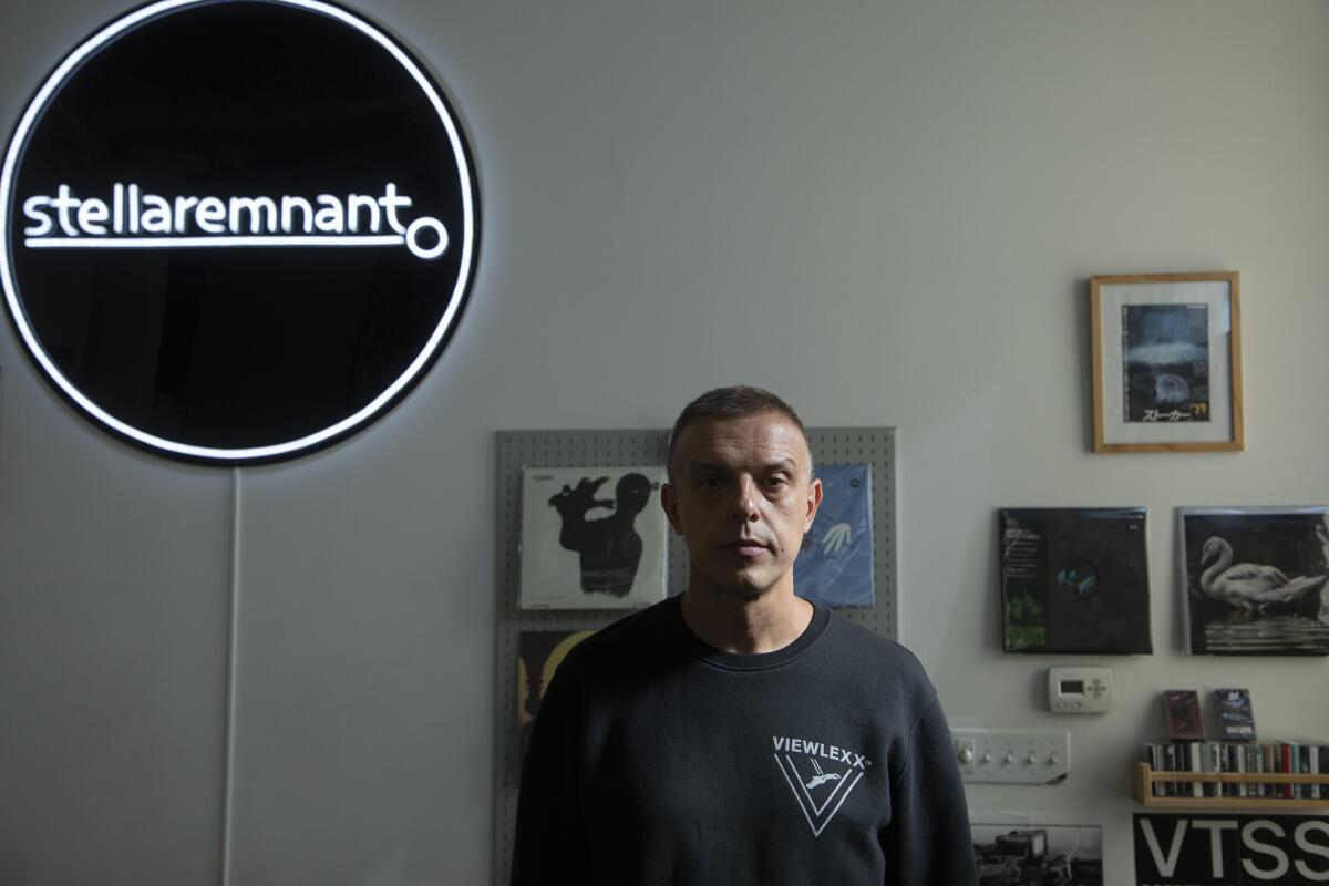 A record-store owner stands beside a neon sign with the name of his store, Stella Remnant.