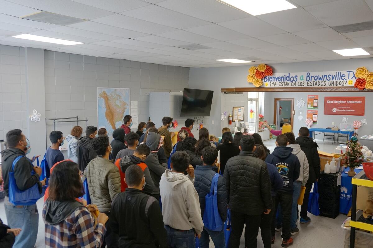 People line up in front of a sign reading, in Spanish, "Welcome to Brownsville, Texas."