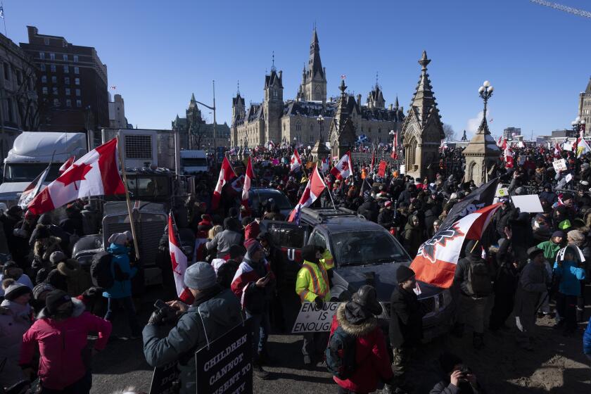 Protestors mingle around vehicles parked on Wellington St. in front of West Block and the Parliament buildings as they participate in a cross-country truck convoy protesting measures taken by authorities to curb the spread of COVID-19 and vaccine mandates in Ottawa on Saturday, Jan. 29, 2022. (Adrian Wyld/The Canadian Press via AP)