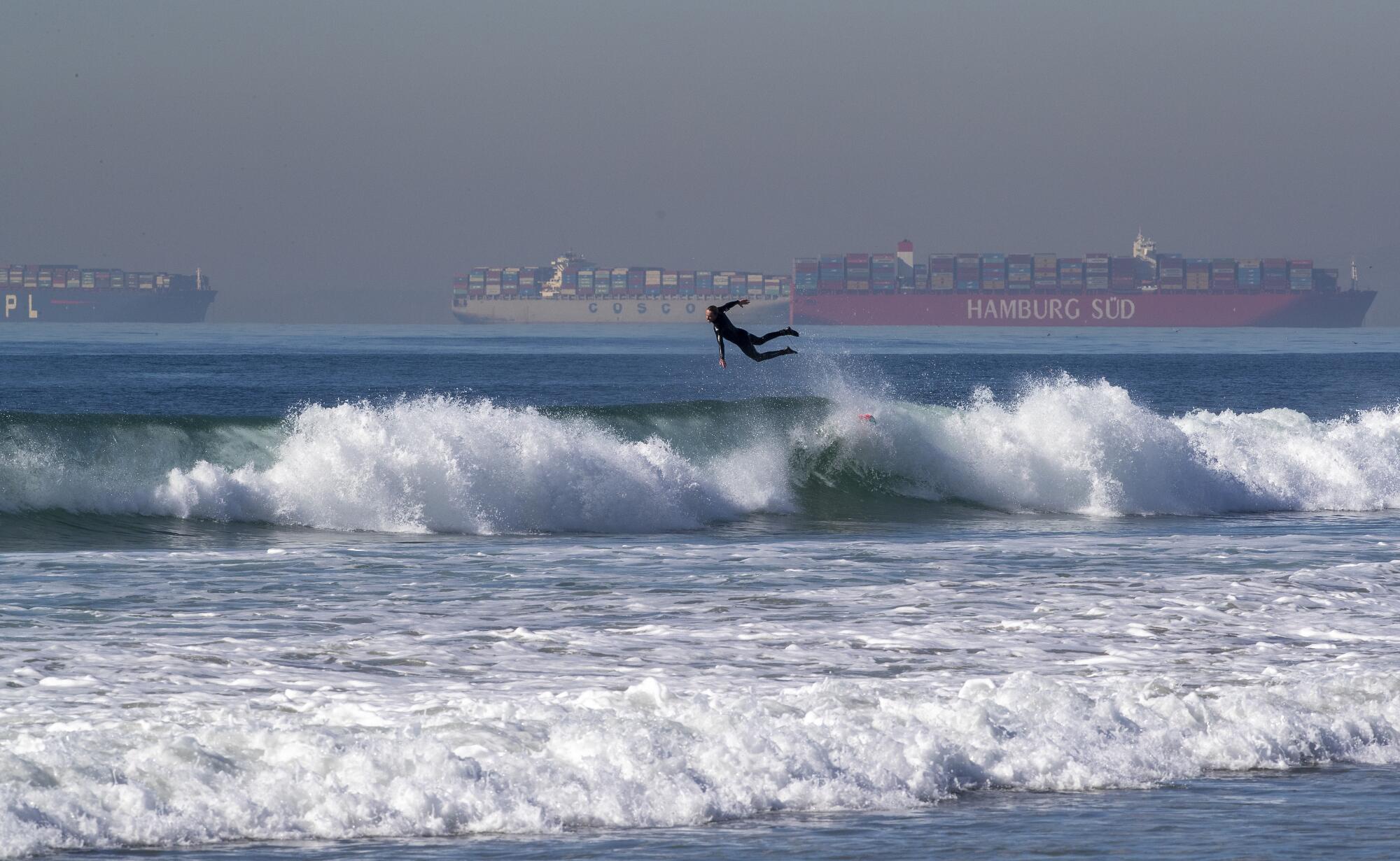 A surfer going airborne with cargo ships in the distance