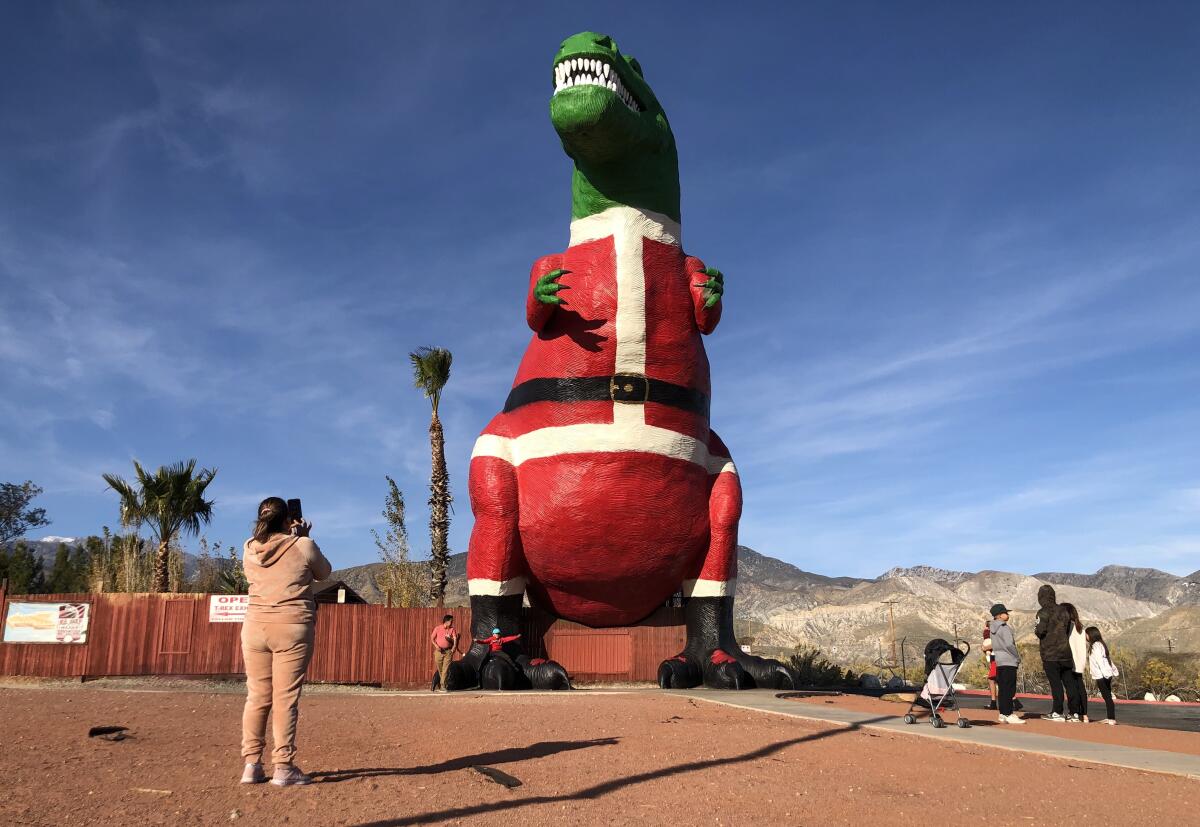 A woman holds up her phone to take a photo of people posing in front of a large concrete T-rex.