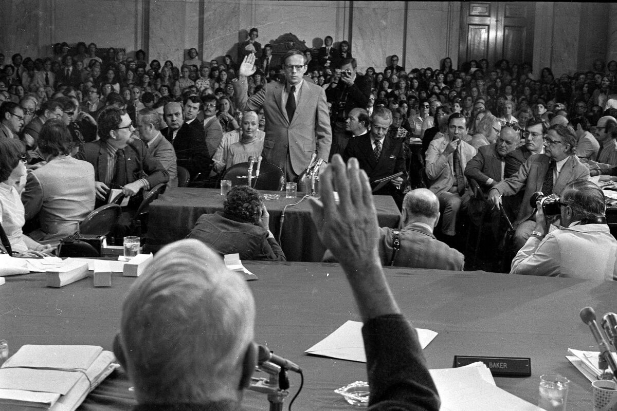 A black and white photo of a man being sworn in to testify before a large group of onlookers