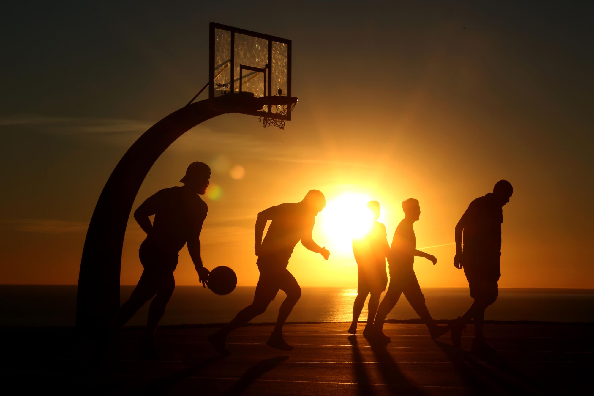 Basketball players are silhouetted against a setting sun 