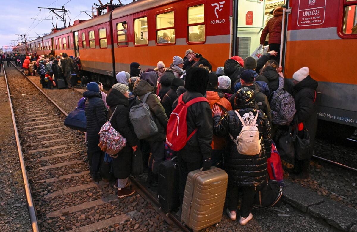 Crowds with luggage and backpacks gather outside train cars, waiting to board 
