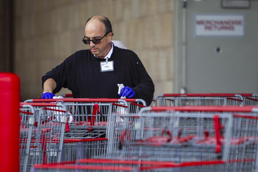 An employee at Costoc in Huntington Beach disenfects shopping carts on Monday, March 16.