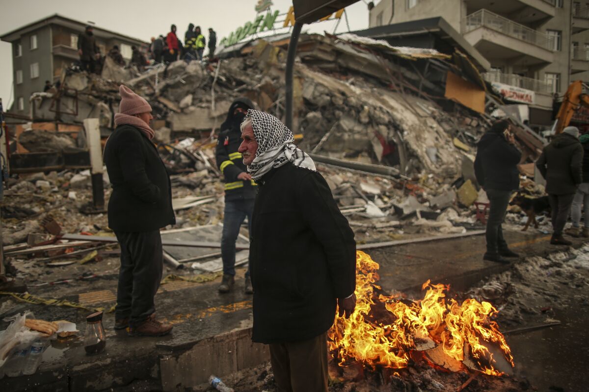 People warming themselves by a fire next to a collapsed building