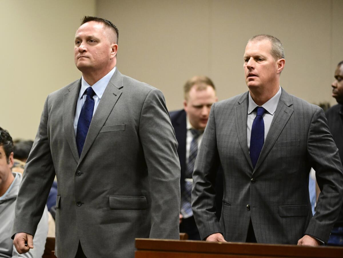 Men in gray suits stand in a courtroom. 