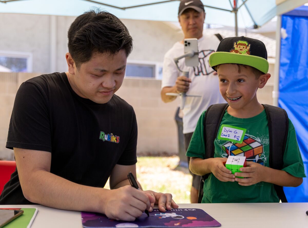 Dylan Garcia looks at his parents while Max Park, the greatest Cuber in the world, signs his autograph at "Day of the Cube."