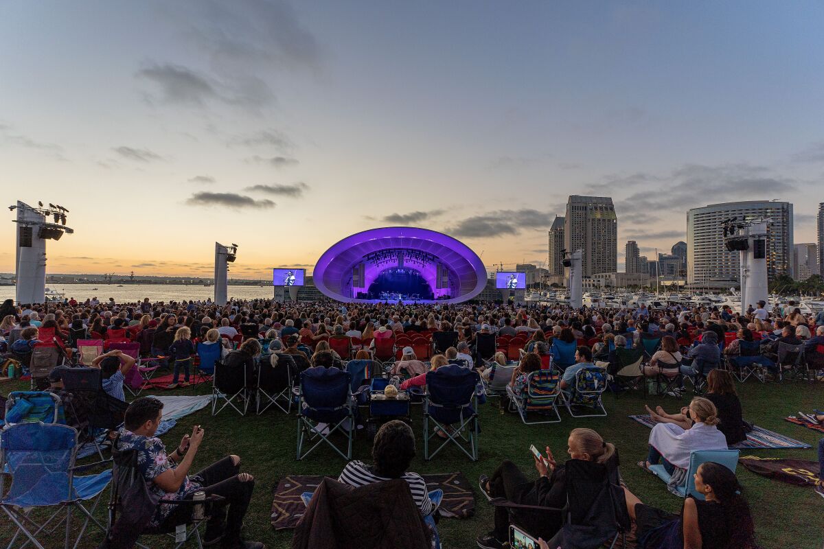 Music fans surround the Rady Shell, lit in purple, at sunset.