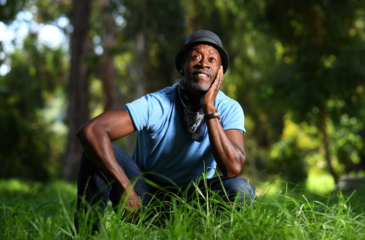 Actor Don Cheadle sitting in the grass among trees.