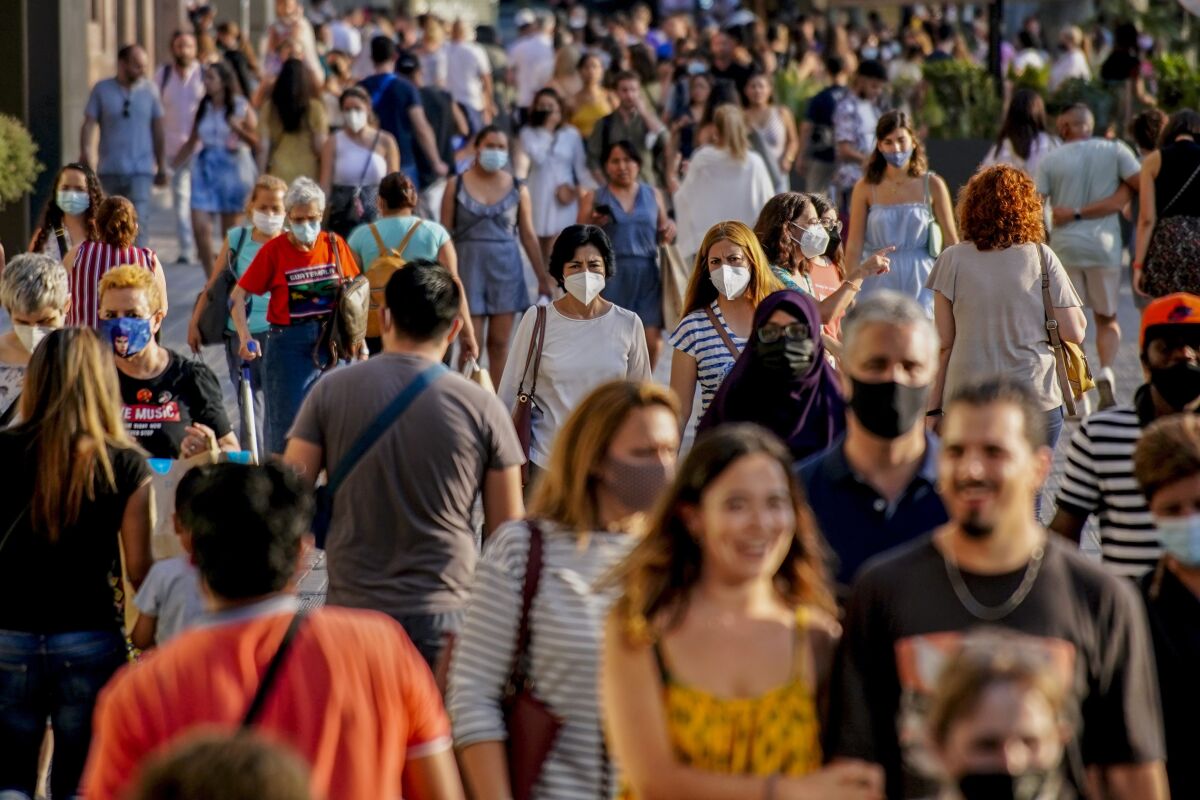 FILE - People wearing a face mask to protect against the spread of coronavirus walk along a street in downtown Barcelona, Spain, July 3, 2021. Some European countries such as Spain are making tentative plans for when they might start treating COVID-19 as an "endemic" disease, but the World Health Organization and other officials have warned that the world is nowhere close to declaring the pandemic over. (AP Photo/Joan Mateu, File)