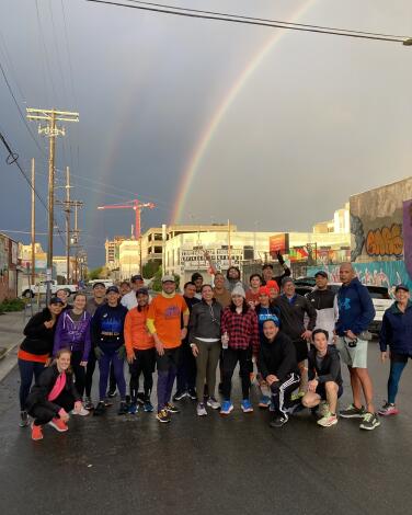 A group of runners outdoors, posing for a photo under a rainbow