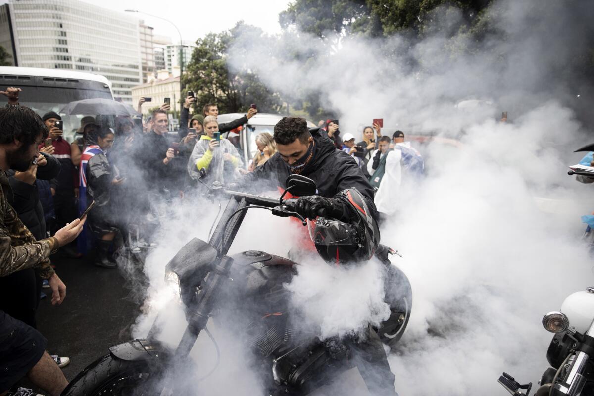 A motorcyclist creates smoke as smiling bystanders record him on their phones