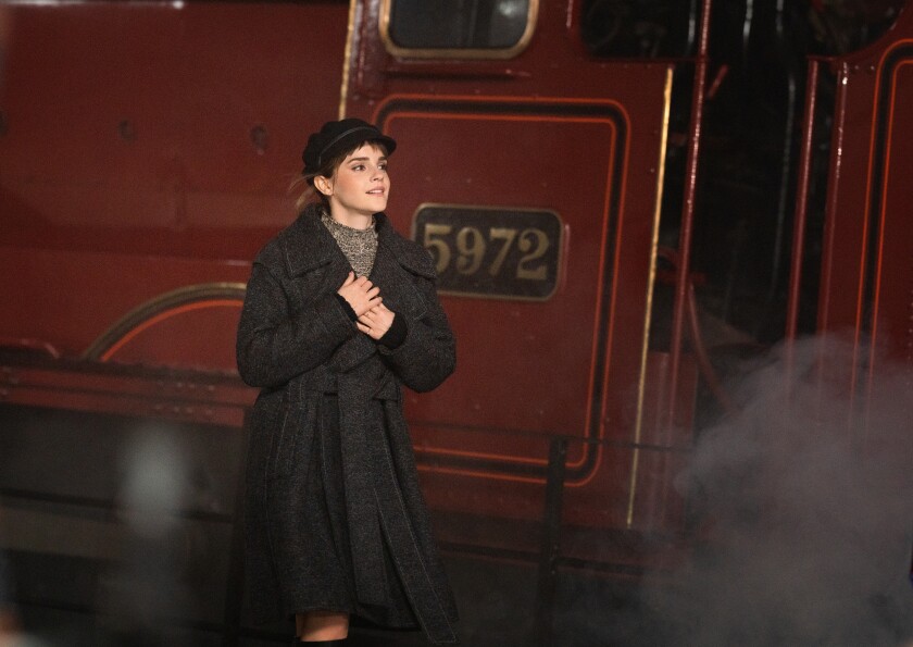 A woman in a hat and coat walking next to a red train.