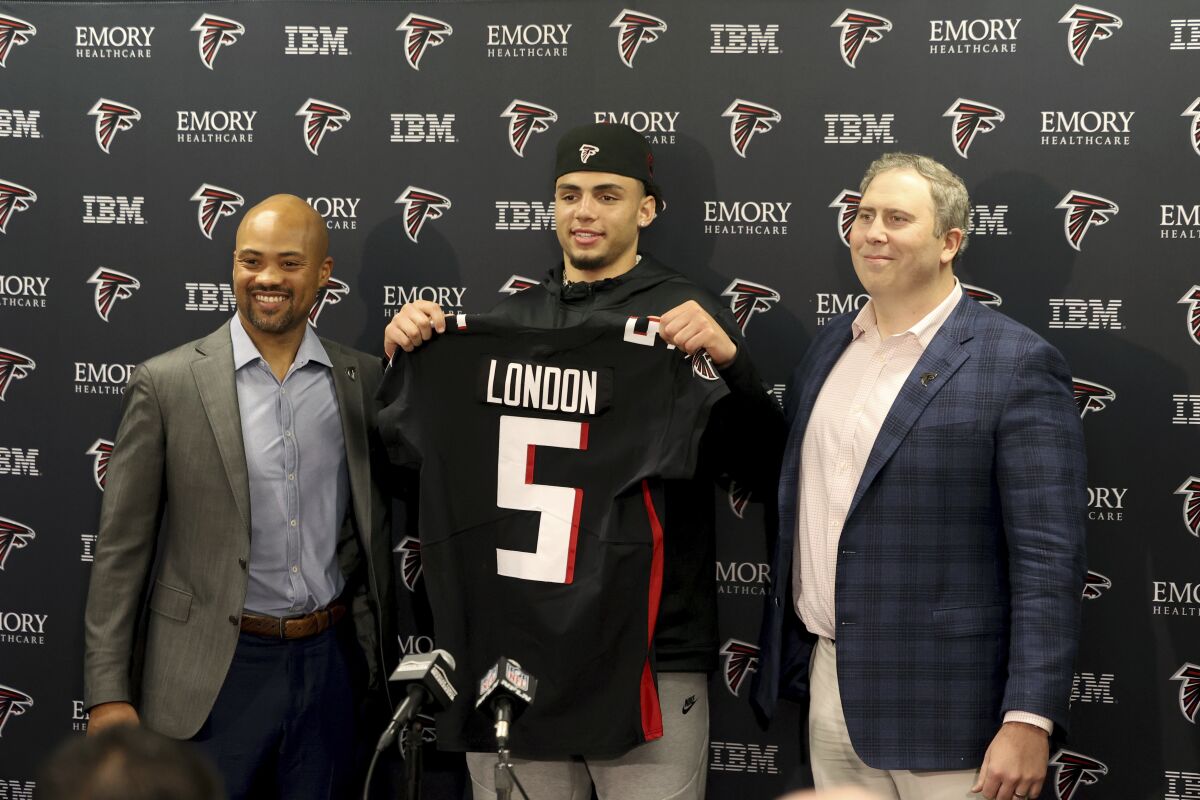 Atlanta Falcons first-round NFL football draft pick Drake London, center, a wide receiver from USC, holds up his jersey with general manager Terry Fontenot, left, and head coach Arthur Smith, right, at the team's practice facility Friday, April 29, 2022, in Flowery Branch, Ga. (Jason Getz/Atlanta Journal-Constitution via AP)
