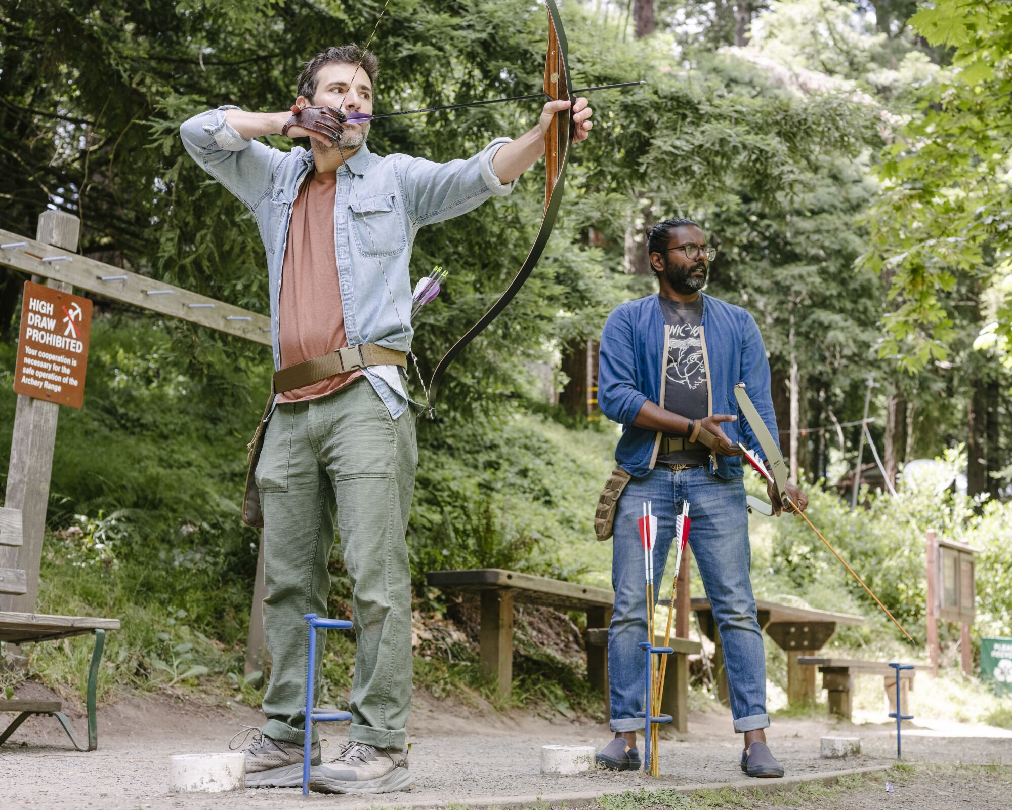 Two men hold bows at an archery range.