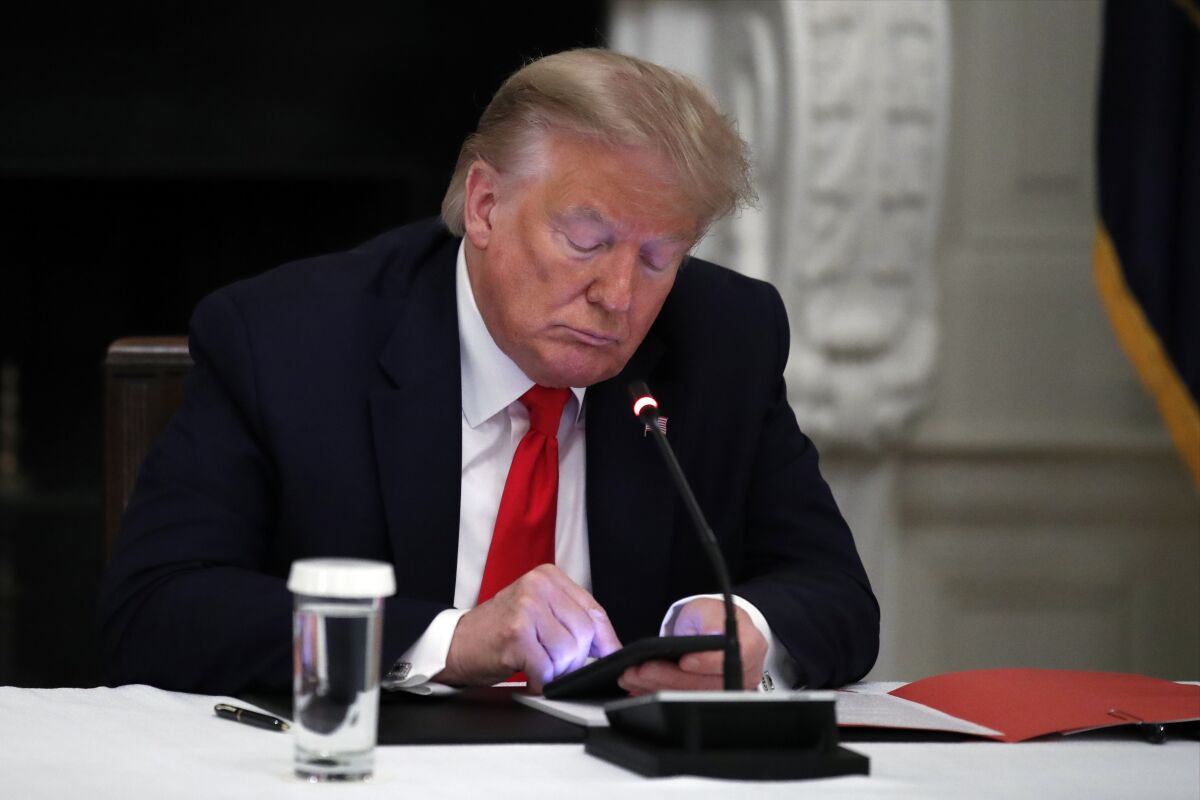 FILE - President Donald Trump looks at his phone during a roundtable with governors on the reopening of America's small businesses, in the State Dining Room of the White House in Washington, June 18, 2020. A San Francisco judge has rejected Trump's lawsuit challenging his lifetime ban from Twitter. U.S. District Judge James Donato said in a ruling Friday, May 6, 2022, that Trump's failed to show Twitter abridged his First Amendment right to free speech. (AP Photo/Alex Brandon, File)