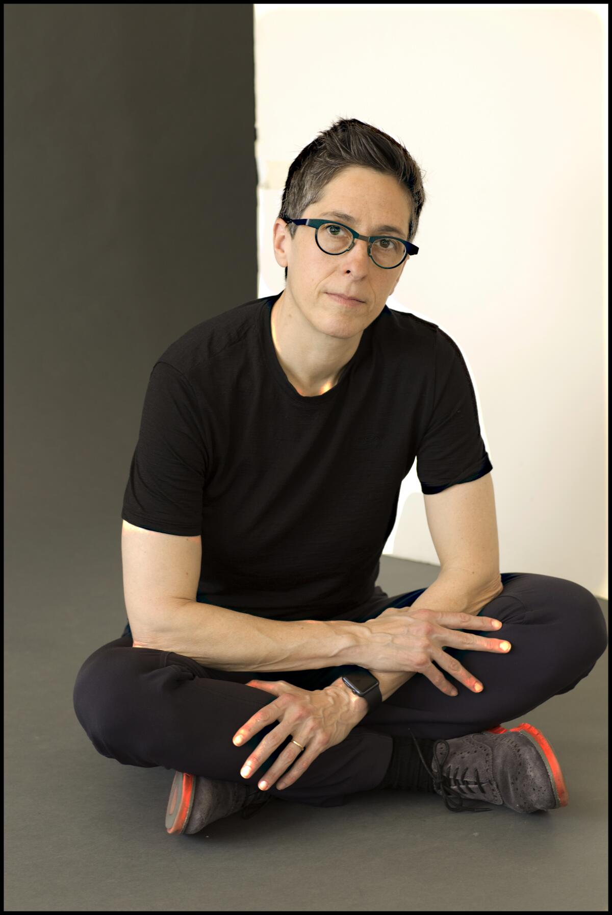 Alison Bechdel wears all black while sitting cross-legged for a portrait.
