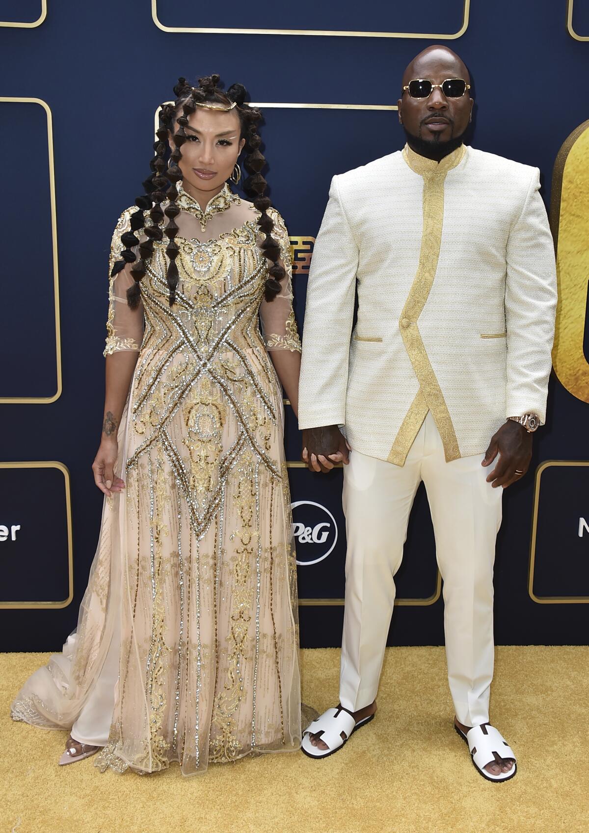 Jeannie Mai Jenkins in intricate gold gown holding hands with Jeezy in a white tunic, pants and sandals