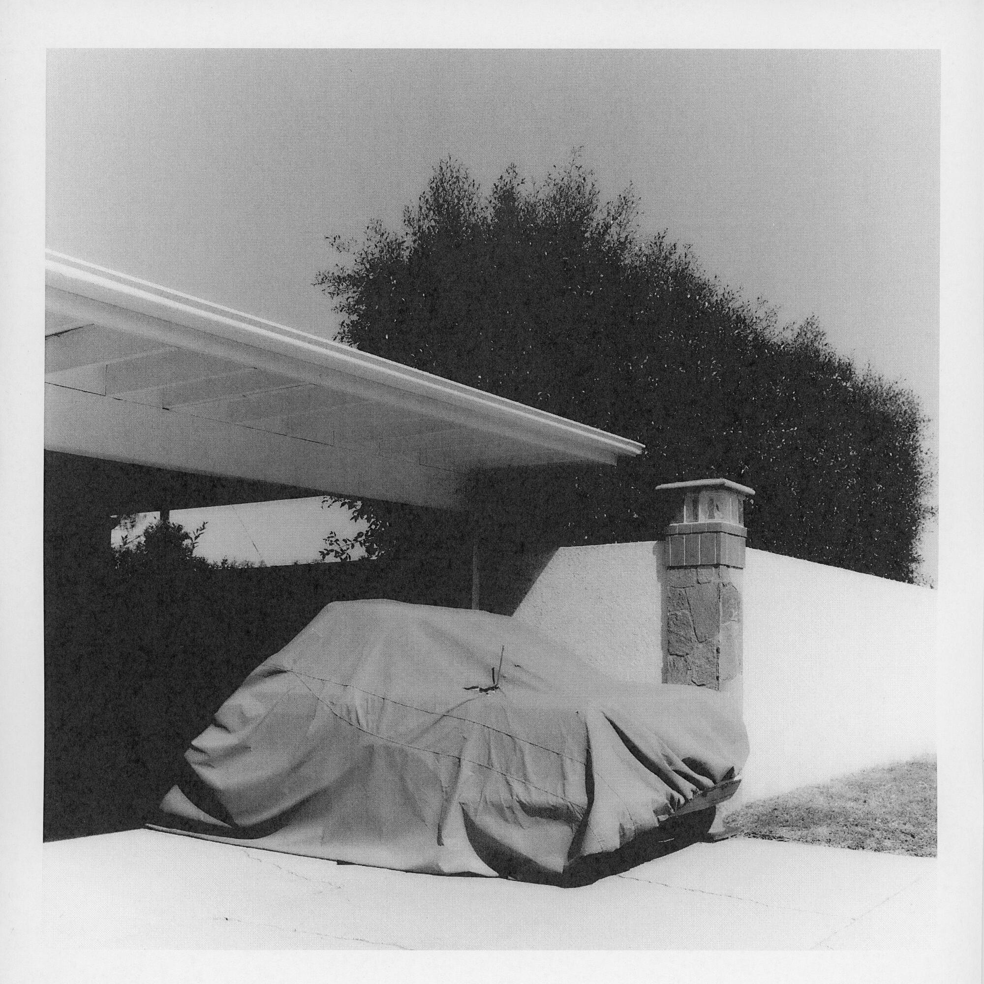 A black-and-white photo of a car parked under an awning.