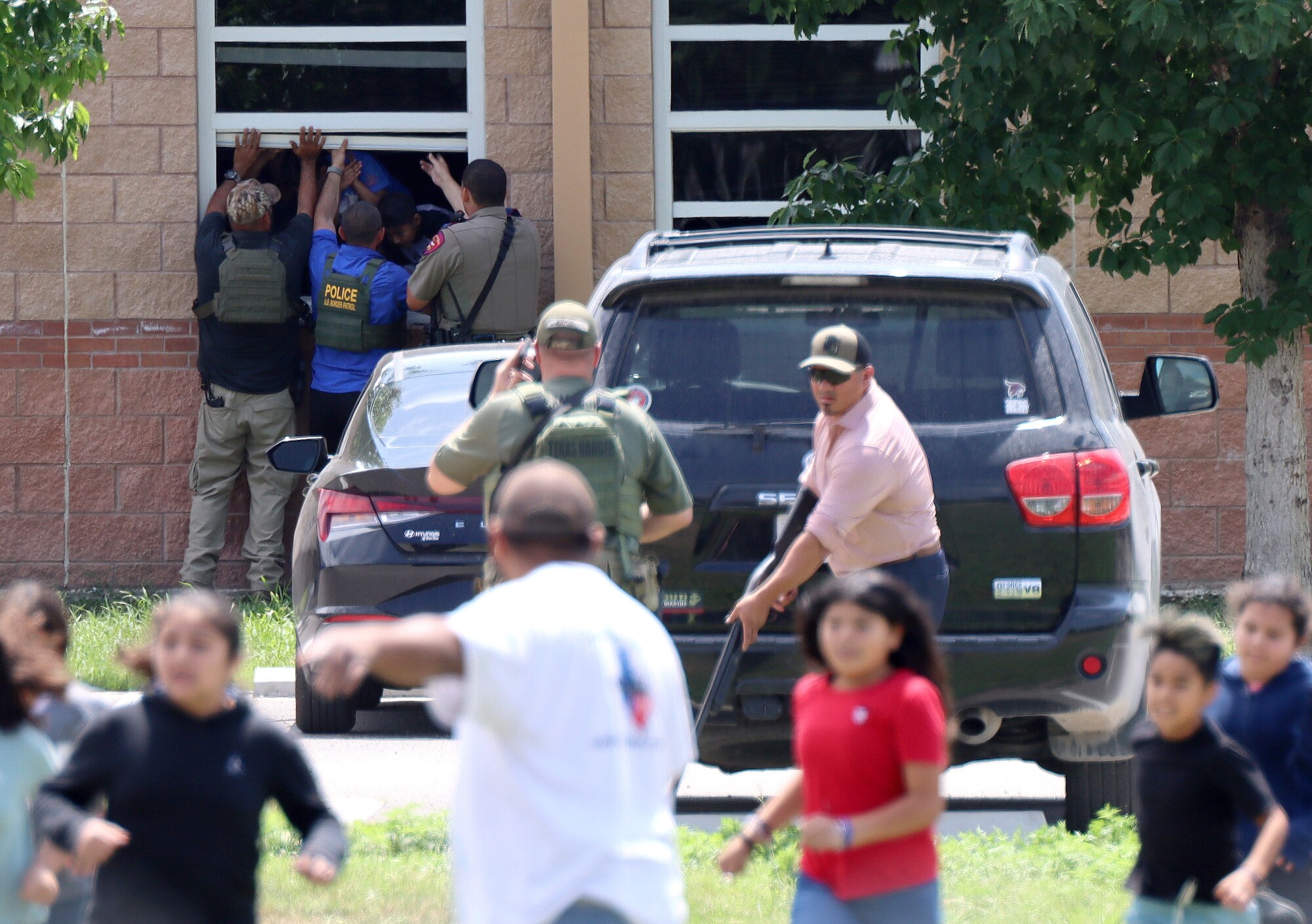 Officers with guns drawn are scene outside Robb Elementary School as students are evacuated out of windows.